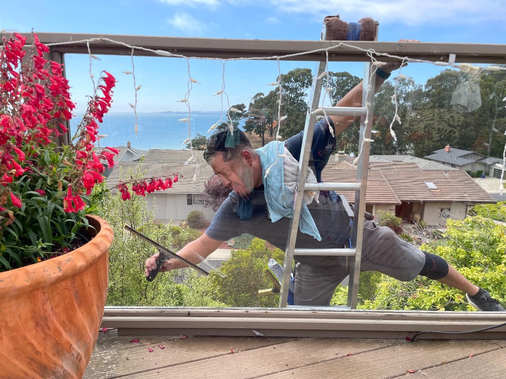 Window cleaner on ladder with squeegee and ocean view in Santa Cruz