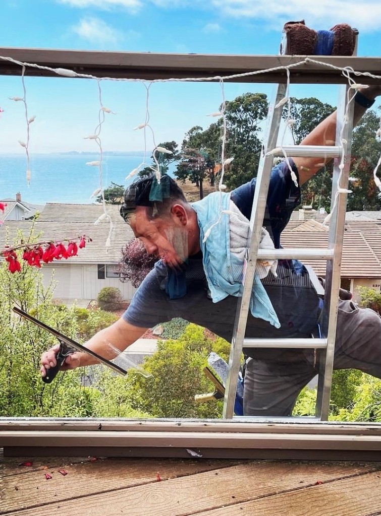 WCSC crew member cleaning windows on ladder with ocean view